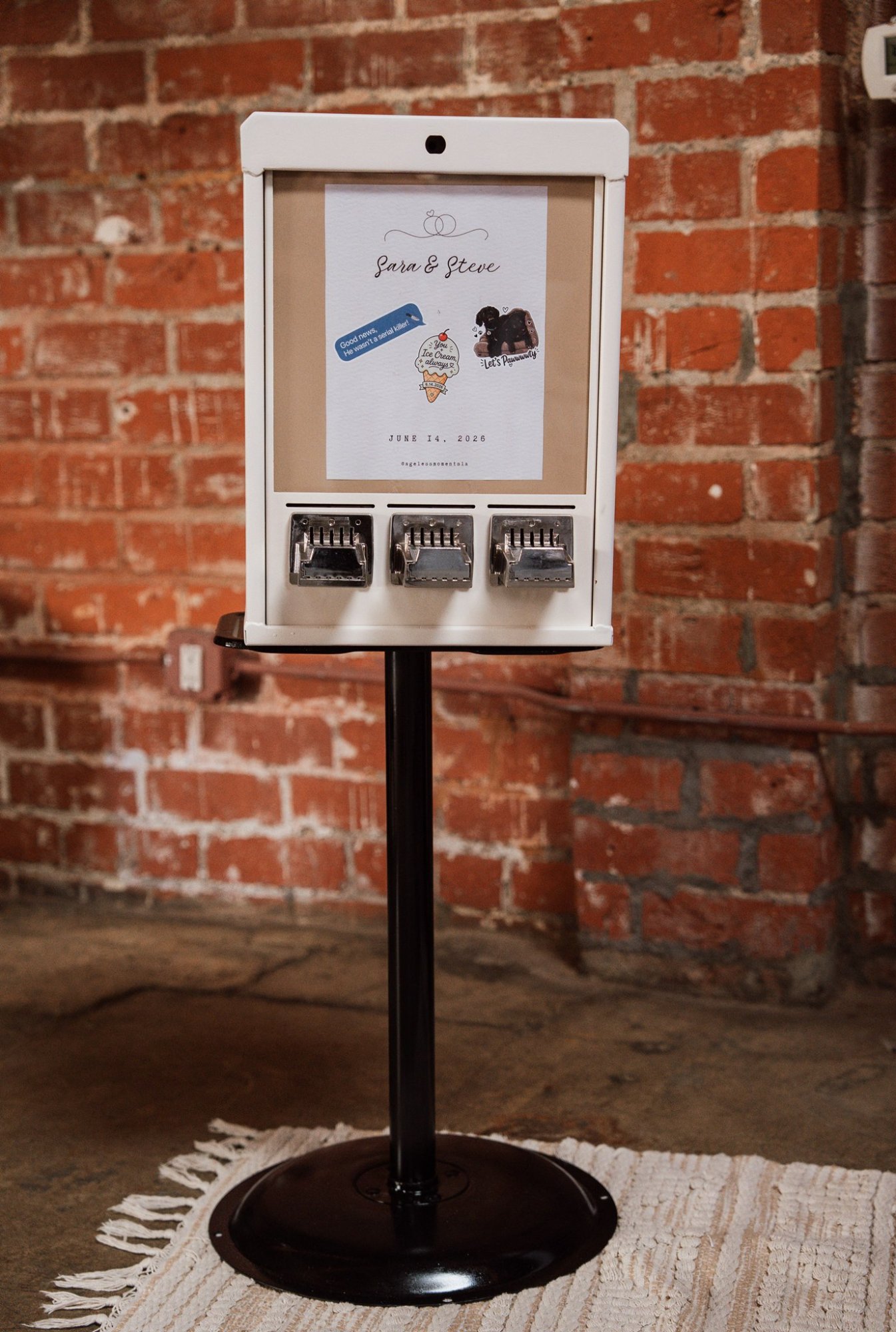 A white machine with three metal dispensers on a stand, against exposed brick wall